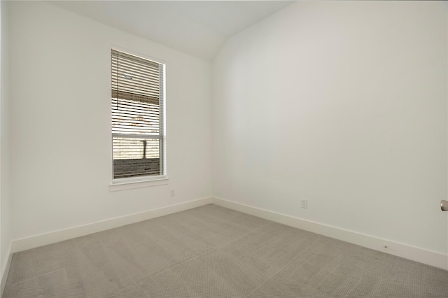 empty room with baseboards, light carpet, and vaulted ceiling