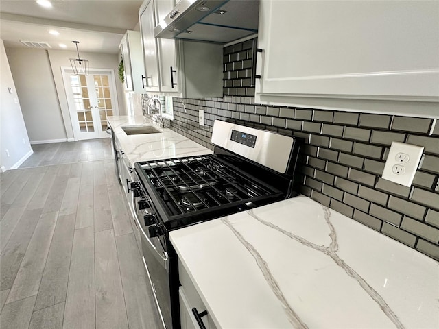 kitchen with a sink, under cabinet range hood, backsplash, wood finished floors, and stainless steel gas range