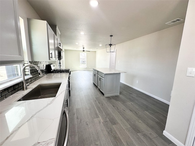 kitchen featuring visible vents, a sink, light stone counters, dark wood-style floors, and stainless steel range with gas cooktop