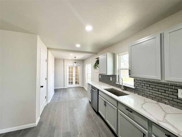 kitchen with a sink, light stone counters, tasteful backsplash, stainless steel dishwasher, and wood finished floors