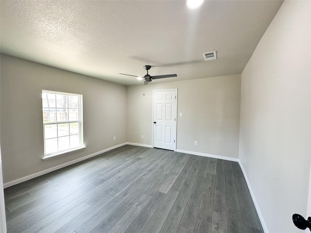 empty room featuring baseboards, visible vents, dark wood finished floors, ceiling fan, and a textured ceiling