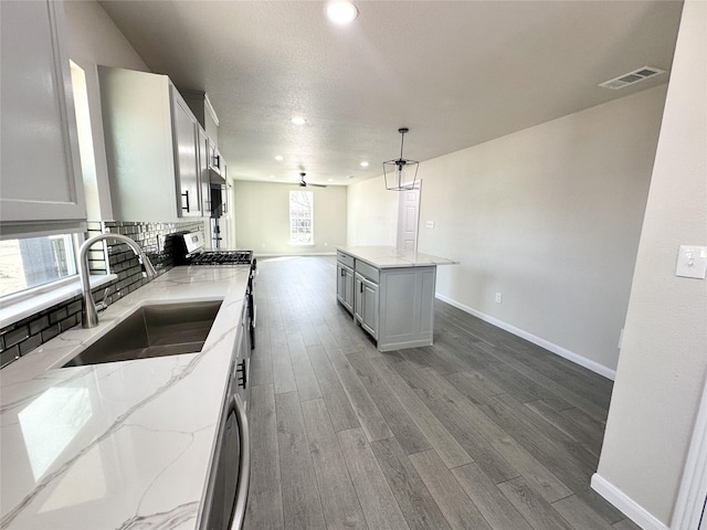 kitchen featuring wood finished floors, visible vents, a sink, decorative backsplash, and gas range