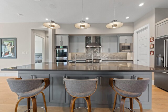 kitchen with dark countertops, appliances with stainless steel finishes, gray cabinetry, and wall chimney range hood