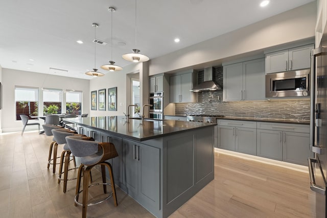 kitchen featuring dark countertops, wall chimney exhaust hood, gray cabinetry, and stainless steel appliances