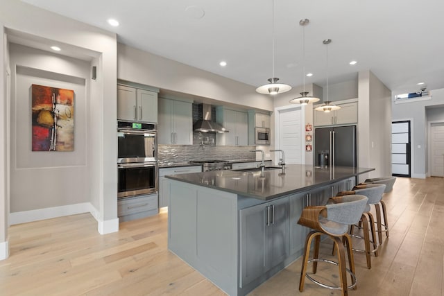 kitchen with a sink, stainless steel appliances, dark countertops, wall chimney range hood, and backsplash