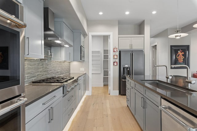 kitchen with light wood-type flooring, a sink, dark countertops, appliances with stainless steel finishes, and wall chimney exhaust hood