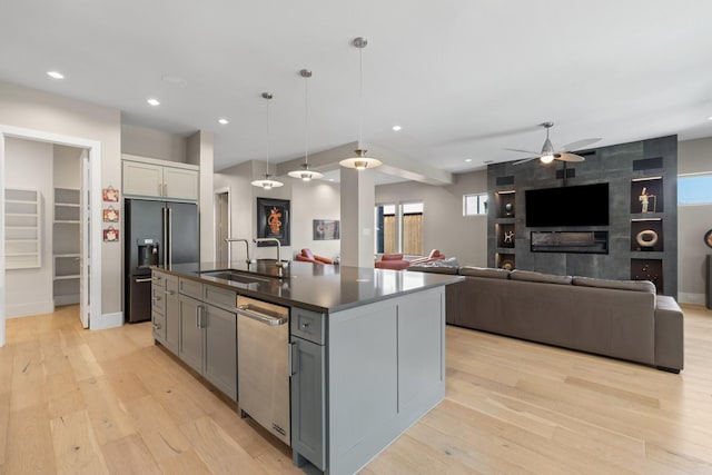 kitchen with dark countertops, an island with sink, light wood-type flooring, high end black refrigerator, and a sink