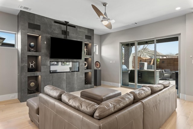 living room featuring visible vents, baseboards, light wood-style floors, and a ceiling fan