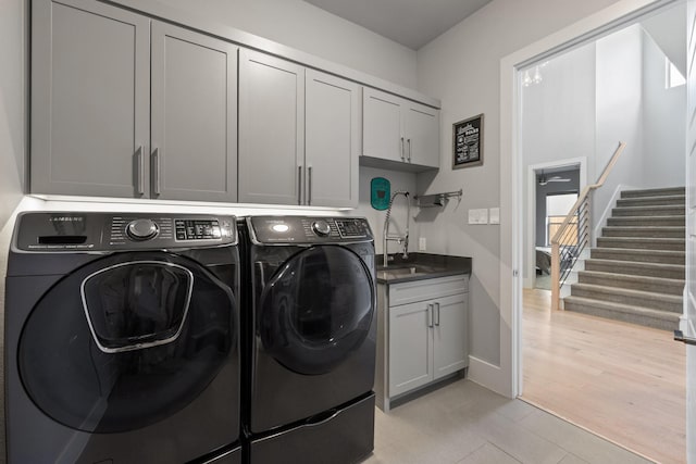 laundry room with a sink, cabinet space, independent washer and dryer, and light wood finished floors