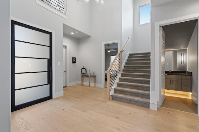 foyer with light wood-type flooring, baseboards, a towering ceiling, and stairway