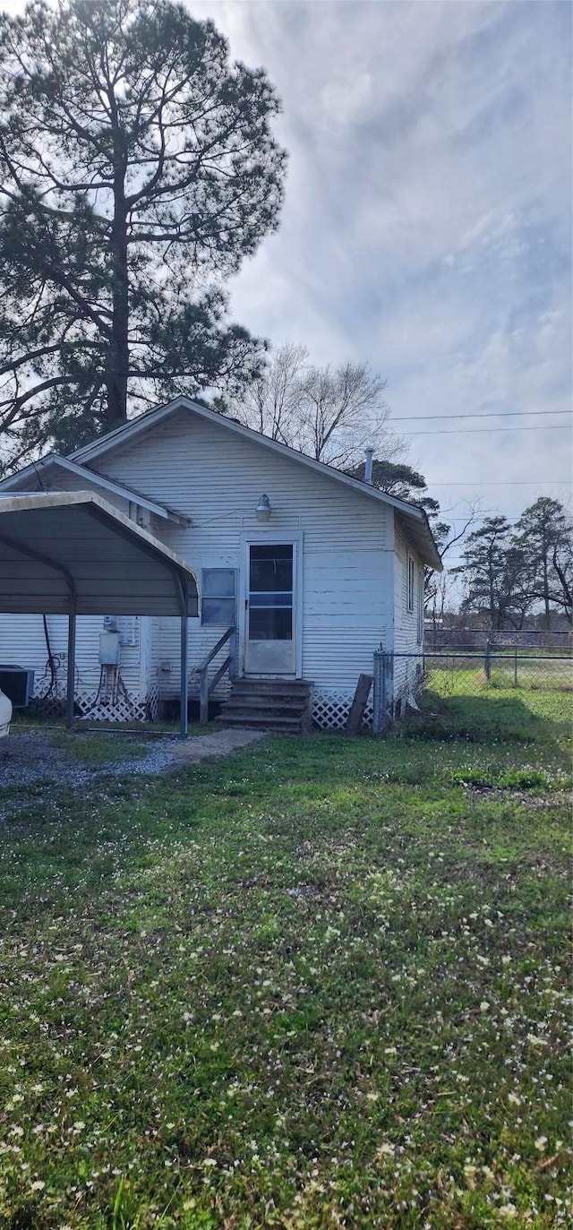 back of house with entry steps, a carport, a lawn, and fence