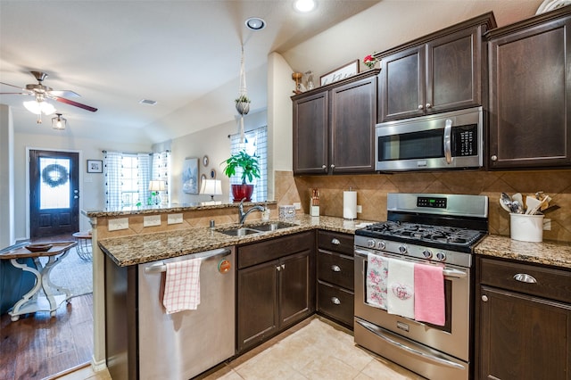 kitchen with a peninsula, a sink, dark brown cabinetry, appliances with stainless steel finishes, and tasteful backsplash