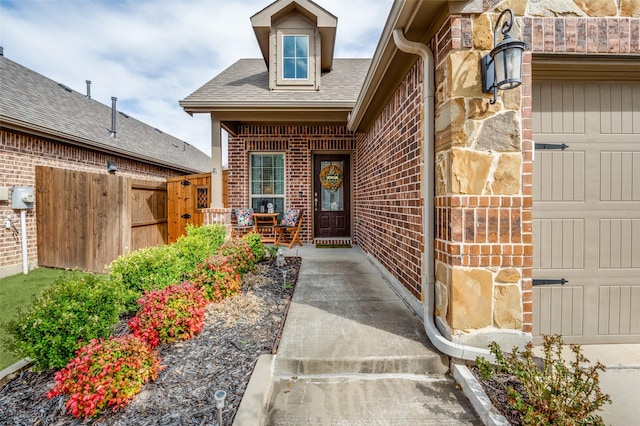 doorway to property featuring covered porch, a garage, fence, and brick siding