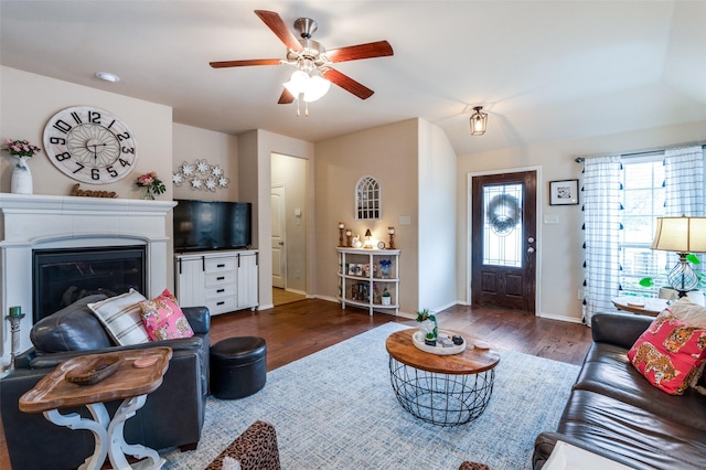 living area with dark wood finished floors, a glass covered fireplace, a ceiling fan, and baseboards