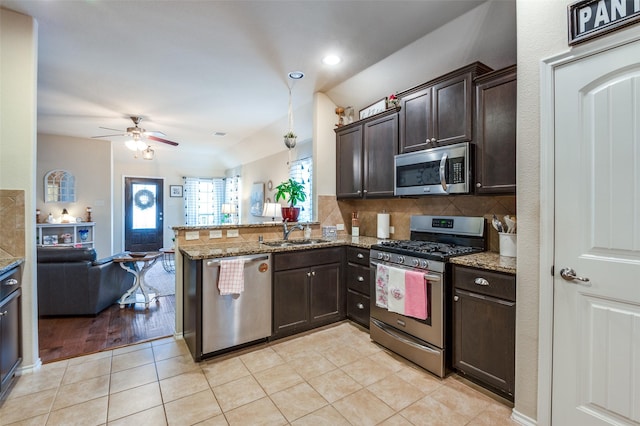 kitchen featuring dark brown cabinetry, light tile patterned floors, appliances with stainless steel finishes, a peninsula, and a sink