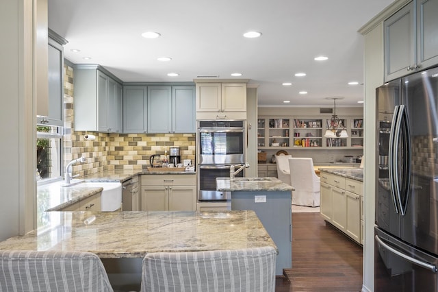 kitchen with light stone counters, dark wood-type flooring, appliances with stainless steel finishes, and a peninsula