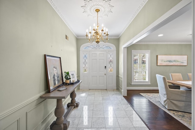 entrance foyer featuring a notable chandelier, a decorative wall, a wainscoted wall, and ornamental molding