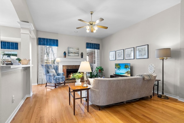 living area with a brick fireplace, light wood-style flooring, baseboards, and ceiling fan