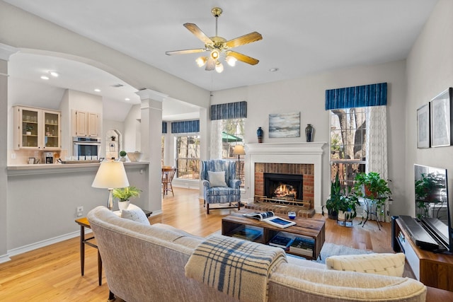 living room featuring a brick fireplace, a healthy amount of sunlight, light wood-style floors, and ceiling fan