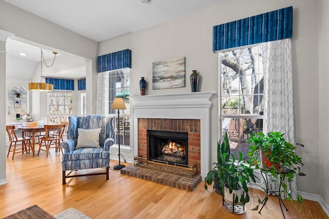 living room with a brick fireplace, baseboards, and wood finished floors