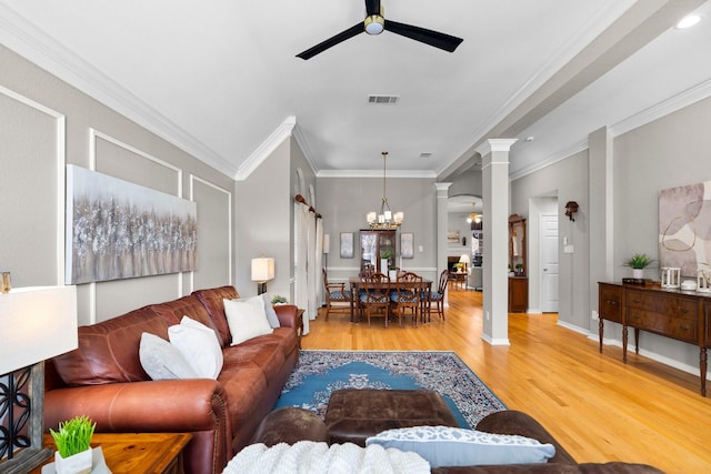 living room with visible vents, crown molding, decorative columns, ceiling fan with notable chandelier, and wood finished floors