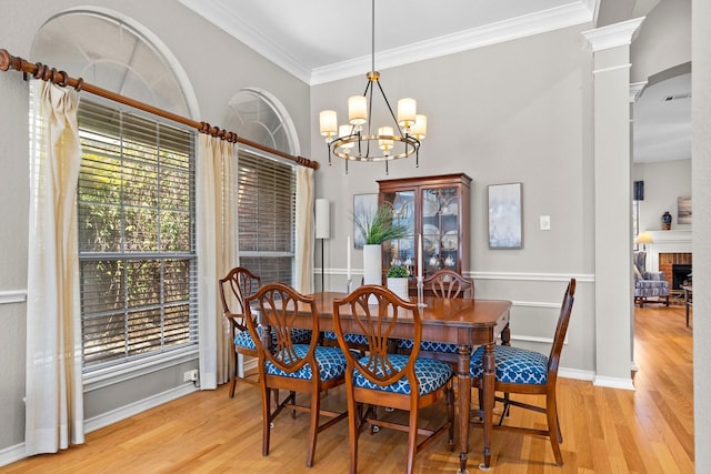 dining area with a brick fireplace, crown molding, baseboards, decorative columns, and wood finished floors