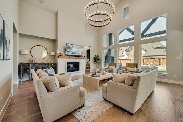 living room with baseboards, wood-type flooring, a high ceiling, and a glass covered fireplace