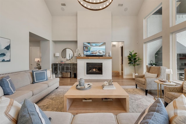 living room with visible vents, a glass covered fireplace, a towering ceiling, wood finished floors, and a notable chandelier