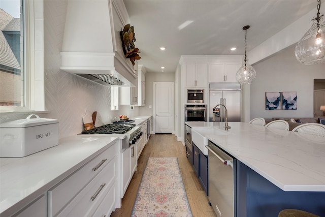 kitchen featuring blue cabinetry, custom range hood, stainless steel appliances, white cabinetry, and a sink