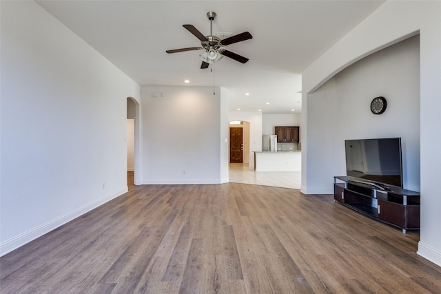 unfurnished living room with a ceiling fan, baseboards, light wood finished floors, recessed lighting, and arched walkways