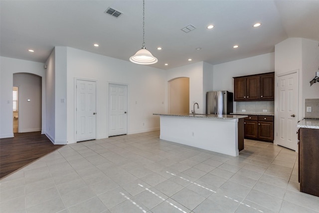 kitchen featuring visible vents, arched walkways, freestanding refrigerator, a sink, and tasteful backsplash