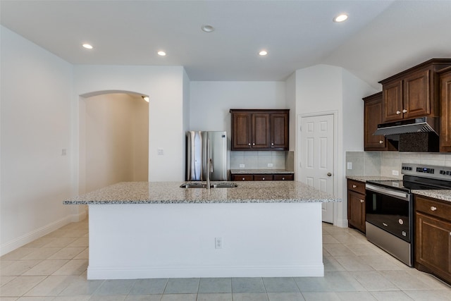 kitchen with under cabinet range hood, light stone countertops, appliances with stainless steel finishes, and an island with sink