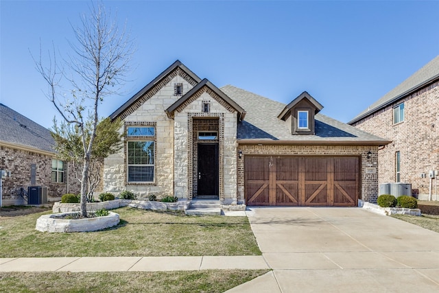 french country home featuring brick siding, a shingled roof, concrete driveway, stone siding, and an attached garage