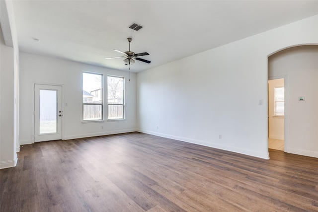 spare room with a ceiling fan, dark wood-style floors, visible vents, baseboards, and arched walkways