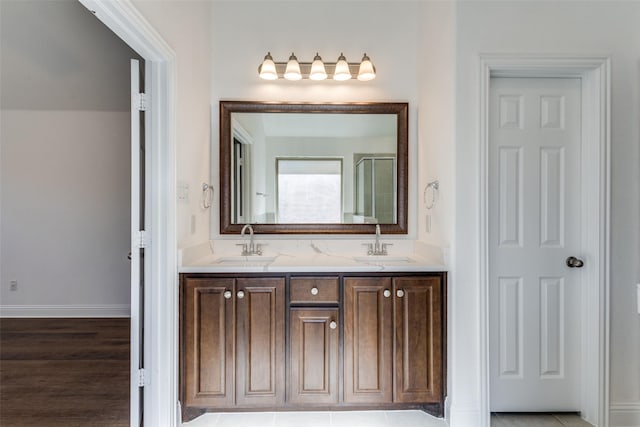 full bathroom featuring double vanity, baseboards, a shower with door, and a sink