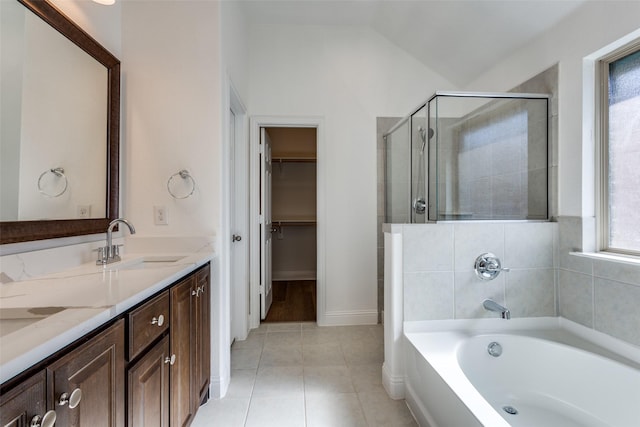 bathroom featuring a walk in closet, a garden tub, a stall shower, a sink, and tile patterned flooring