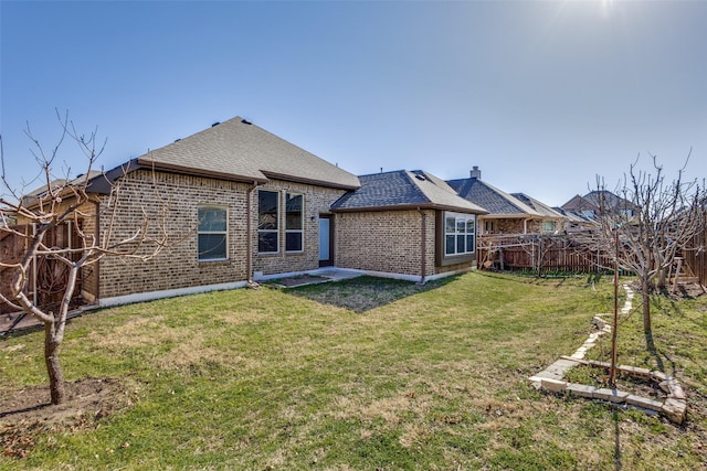 back of house featuring a fenced backyard, brick siding, roof with shingles, and a lawn