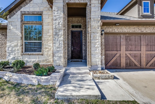 entrance to property with stone siding, an attached garage, brick siding, and roof with shingles