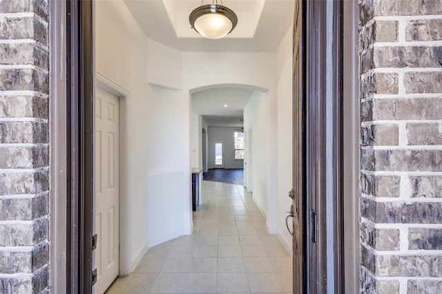 hallway featuring light tile patterned floors, baseboards, and arched walkways