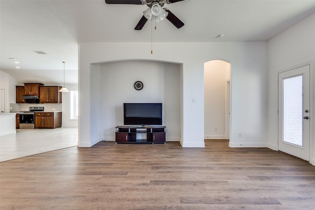 unfurnished living room with a ceiling fan, baseboards, visible vents, light wood-style flooring, and arched walkways