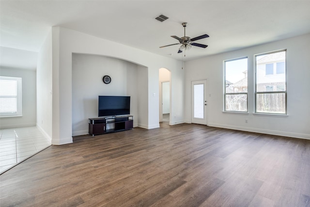 unfurnished living room featuring baseboards, visible vents, arched walkways, ceiling fan, and dark wood-type flooring