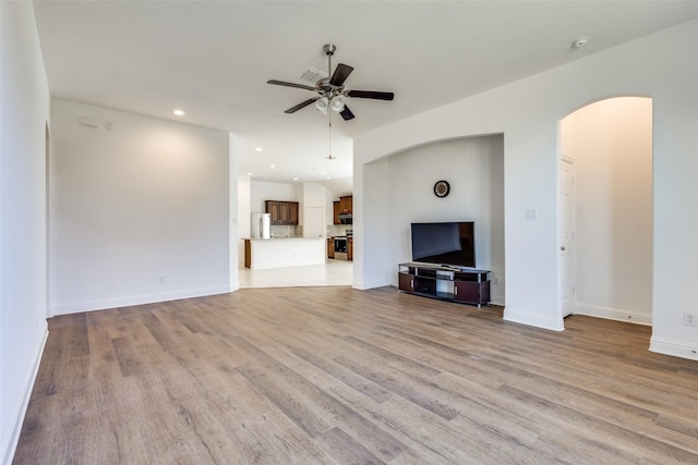 unfurnished living room featuring light wood-type flooring, a ceiling fan, recessed lighting, arched walkways, and baseboards