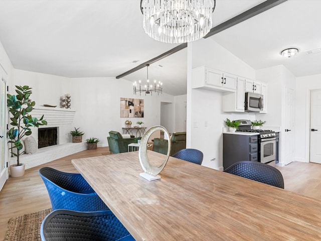 dining area with an inviting chandelier, lofted ceiling with beams, a brick fireplace, and light wood-type flooring