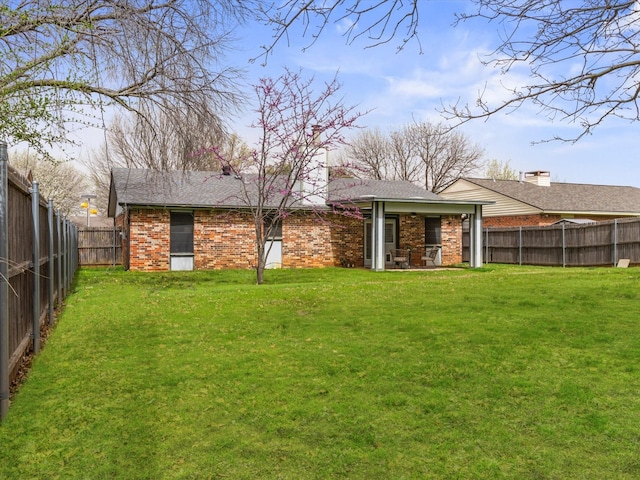 rear view of property featuring brick siding, a lawn, a patio, and a fenced backyard