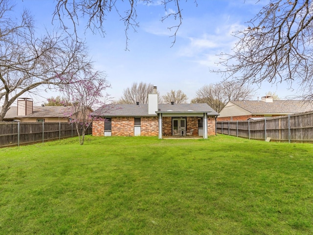 rear view of house featuring a patio area, a lawn, a chimney, and a fenced backyard