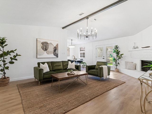 living area featuring wood finished floors, visible vents, an inviting chandelier, vaulted ceiling with beams, and a brick fireplace