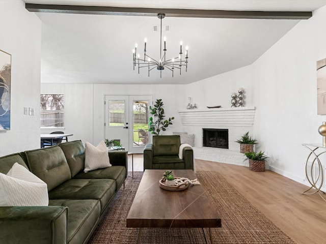 living area featuring visible vents, a notable chandelier, wood finished floors, a fireplace, and vaulted ceiling with beams