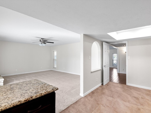 unfurnished living room with arched walkways, light colored carpet, baseboards, and ceiling fan