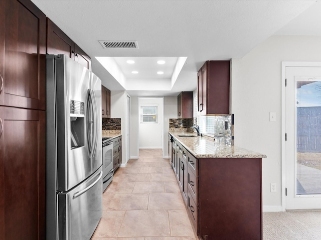 kitchen with a tray ceiling, tasteful backsplash, appliances with stainless steel finishes, and a sink