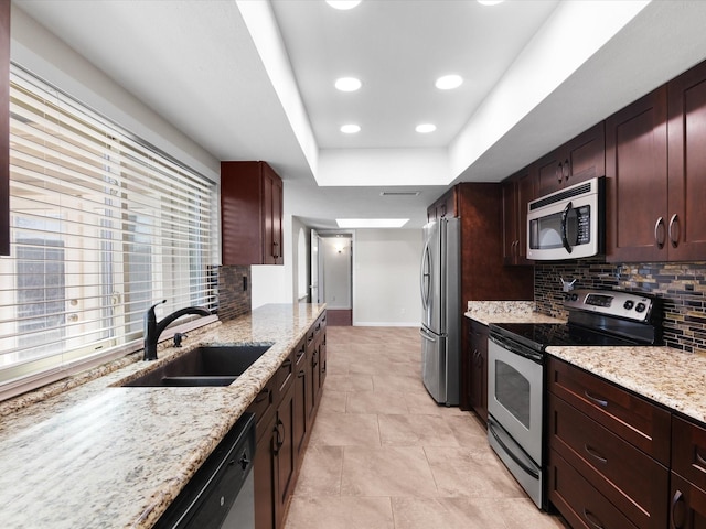 kitchen featuring a sink, backsplash, appliances with stainless steel finishes, a raised ceiling, and light stone countertops